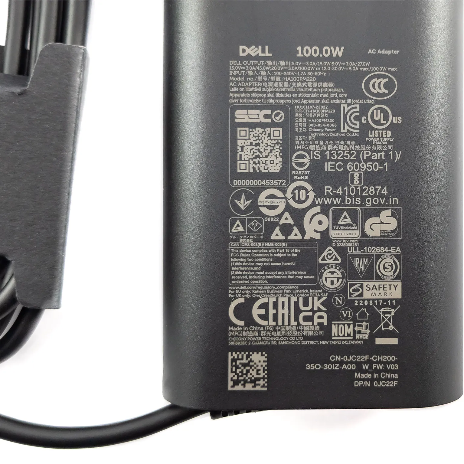 Detailed specification label view of the black Dell 100W USB-C AC power adapter (Model: HA100PM220) displaying 20V/5A, 15V/3A, 9V/3A, and 5V/3A output ratings, DP/N JC22F, regulatory compliance logos, and serial barcodes.